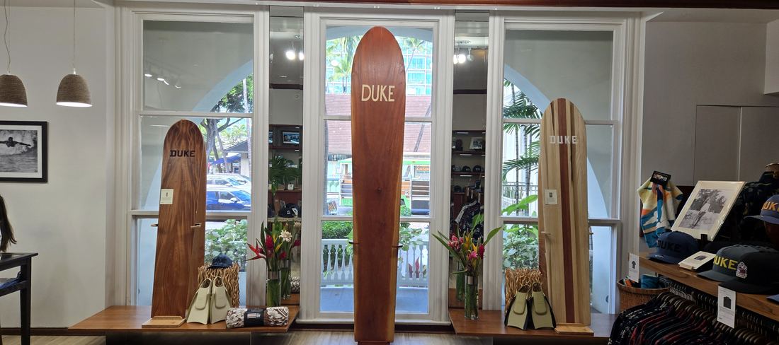 The window bay: three wooden boards standing in tall arched windows, the tallest marked DUKE, with flowers on the ledges.