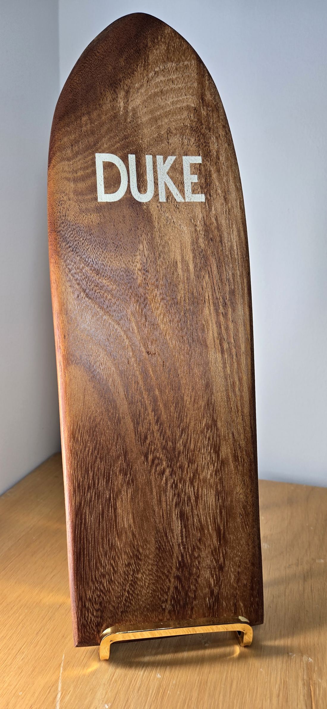 A koa mini board marked DUKE on a brass stand.