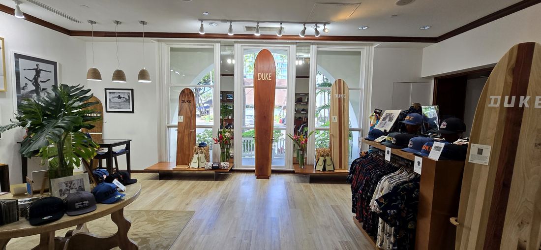 The gallery from the back: a round table of caps, a monstera, shirts on the rail and boards in the windows.